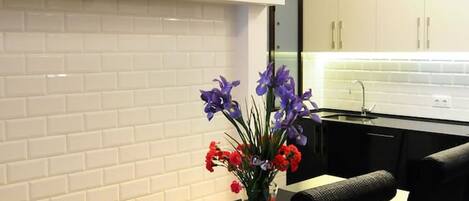 A modern kitchen with white subway tiles, a black countertop, and a dining area with a black chair and a vase of flowers.