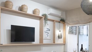 A modern dining area with a round table, white chairs, a television mounted on a wooden shelf, and an air conditioning unit. - Vicens Gem Private Terrace HS Wi-fi in Gracia by Myrentalhost (Barcelona)