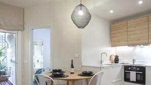 A modern kitchen with white cabinets, a wooden dining table, and two white chairs. - Vicens Gem Private Terrace HS Wi-fi in Gracia by Myrentalhost (Barcelona)