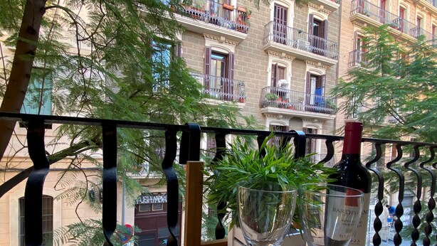 A balcony with a wooden table, two wine glasses, and a bottle of wine.