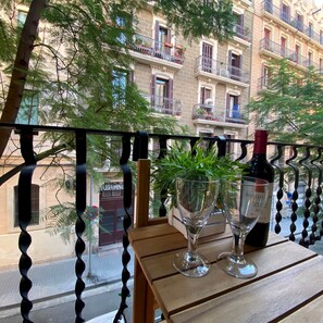 Un balcon avec une table en bois, deux verres à vin et une bouteille de vin.