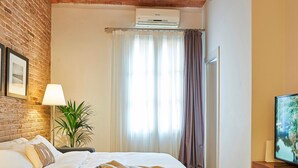 A hotel room with a brick wall, a bed with a beige blanket, a plant, a TV, and an air conditioning unit. - Charming Modern Apt in Trendy Gracia 5PP by Myrentalhost (Barcelona)