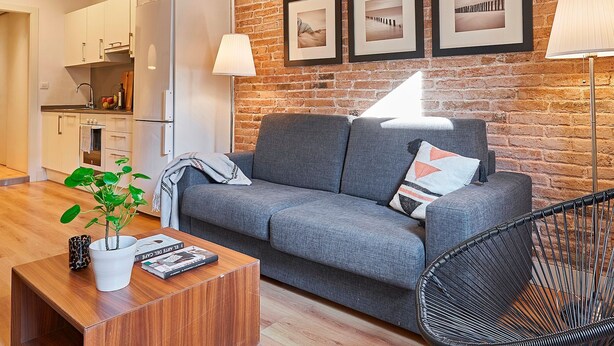 A modern living room with a grey sofa, a coffee table, and a black chair. There is a brick wall with framed pictures and a lamp. - Charming Modern Apt in Trendy Gracia 5PP by Myrentalhost (Barcelona)