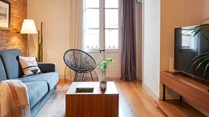 A living room with a sofa, a coffee table, a TV, and a window with curtains. - Charming Modern Apt in Trendy Gracia 5PP by Myrentalhost (Barcelona)
