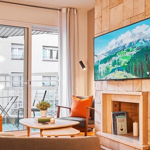 A modern living room with a fireplace, a television mounted on the wall, and a balcony with a view of buildings. - Love Local Life Near Sagrada Familia By Myrentalhost (Barcelona)