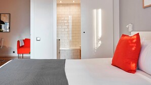 A modern hotel room with a bed, a red chair, a bathroom with a shower, and a white wall with a picture frame. - Love Local Life Near Sagrada Familia By Myrentalhost (Barcelona)