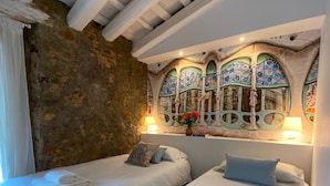 Ein Hotelzimmer mit zwei Betten, einer Steinwand und einem Buntglasfenster.
