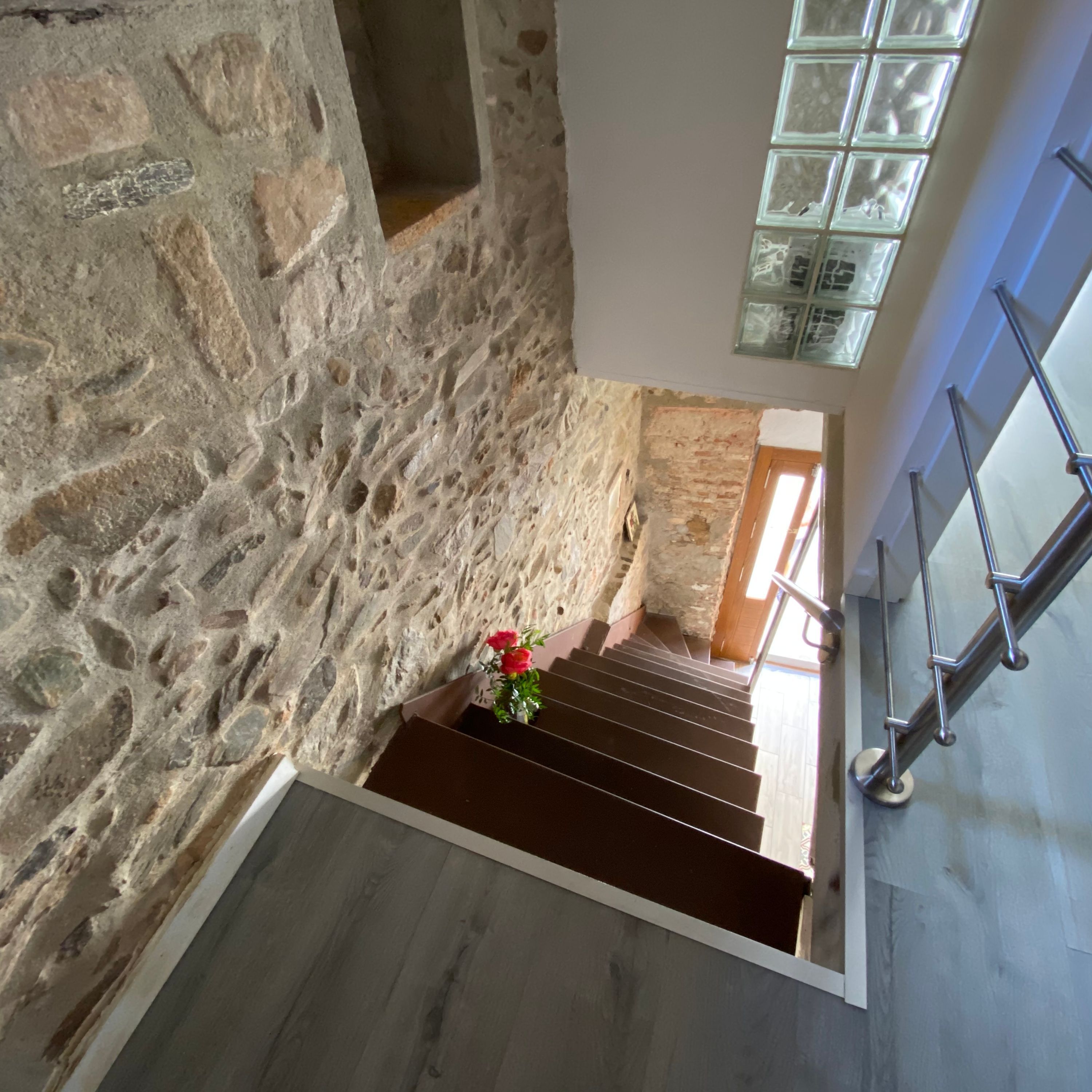 A stone staircase with a wooden handrail and a flower vase at the bottom.