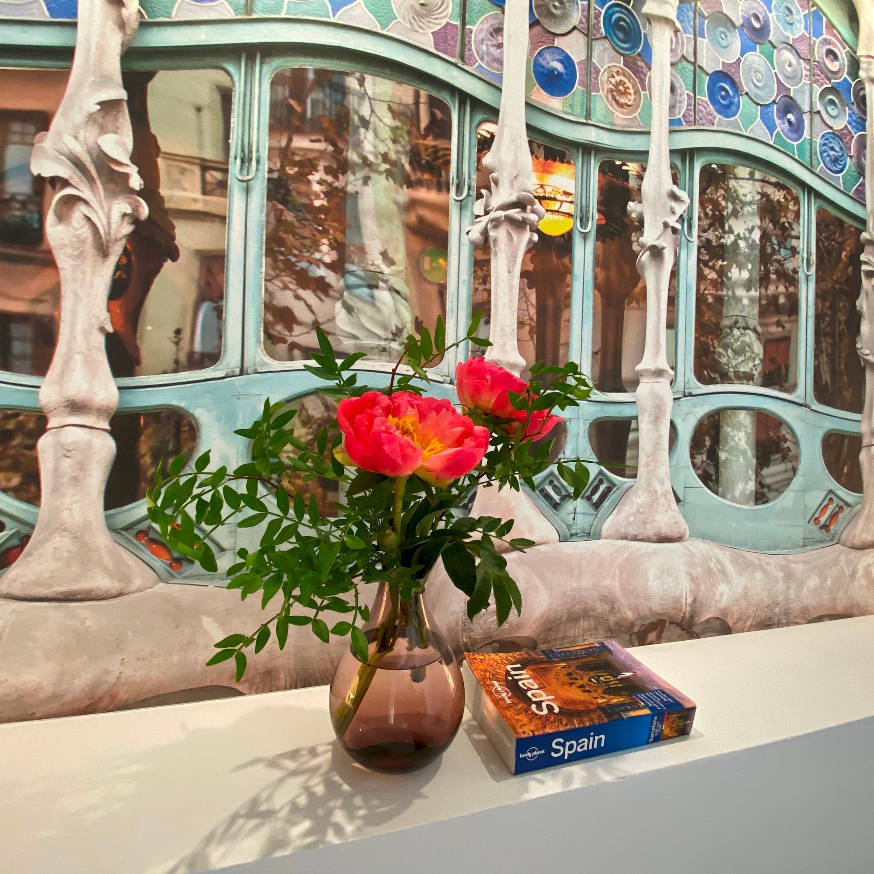 Eine Vase mit Blumen und ein Buch mit dem Titel 'Spain' auf einer Fensterbank.