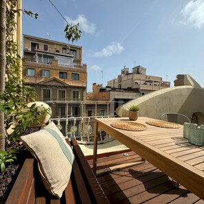 Una terraza de madera con una mesa, cojines y una maceta.