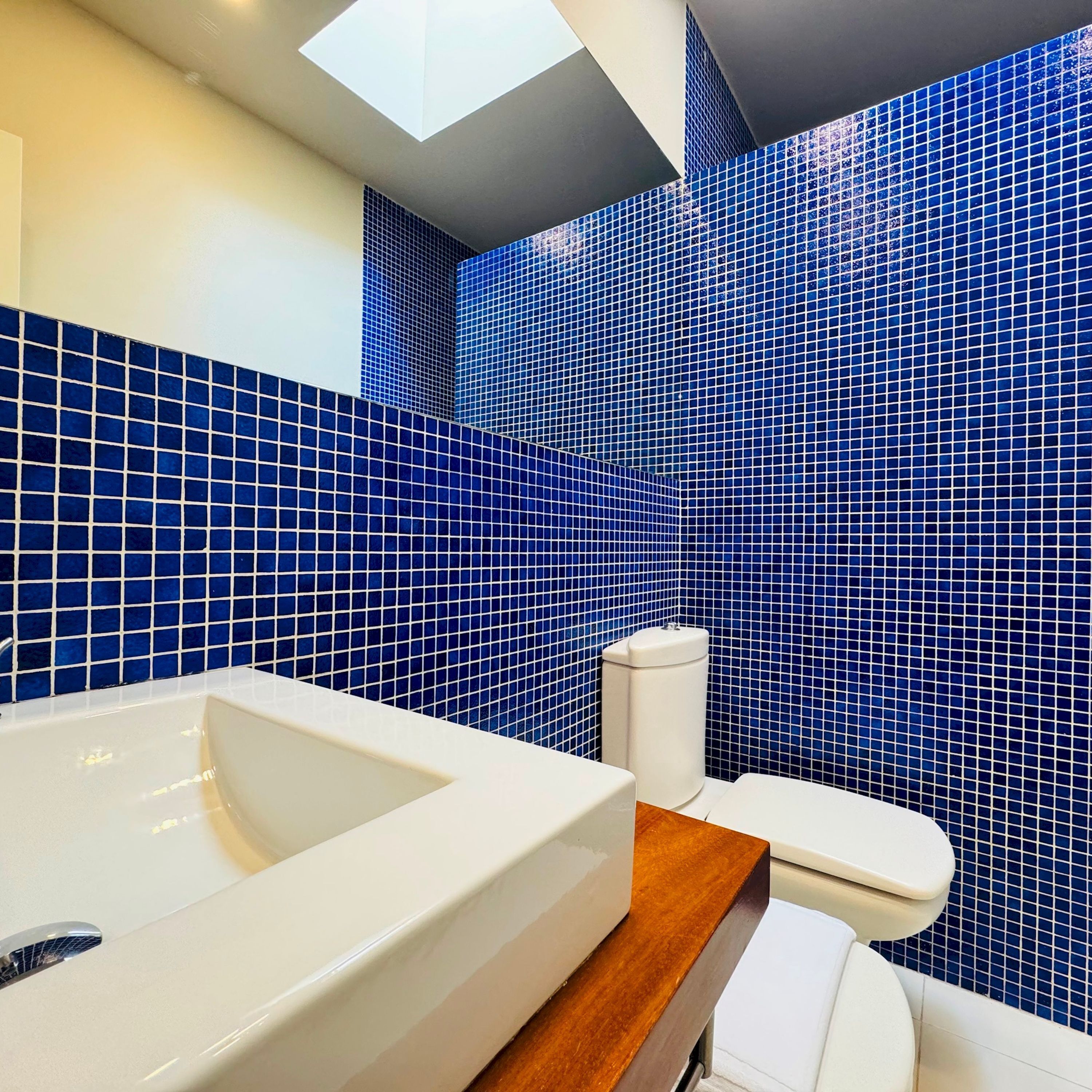 A bathroom with a large bathtub, a toilet, and blue mosaic tiles on the walls.