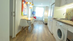 Een moderne keuken met een wasmachine, een eethoek met stoelen en een kleurrijk schilderij aan de muur.