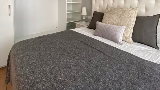 Een slaapkamer met een groot bed, een gestuwd hoofdeinde, een kledingkast met veel planken en een nachtkastje met een lamp.