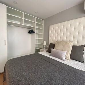 Een slaapkamer met een groot bed, een gestuwd hoofdeinde, een kledingkast met veel planken en een nachtkastje met een lamp.