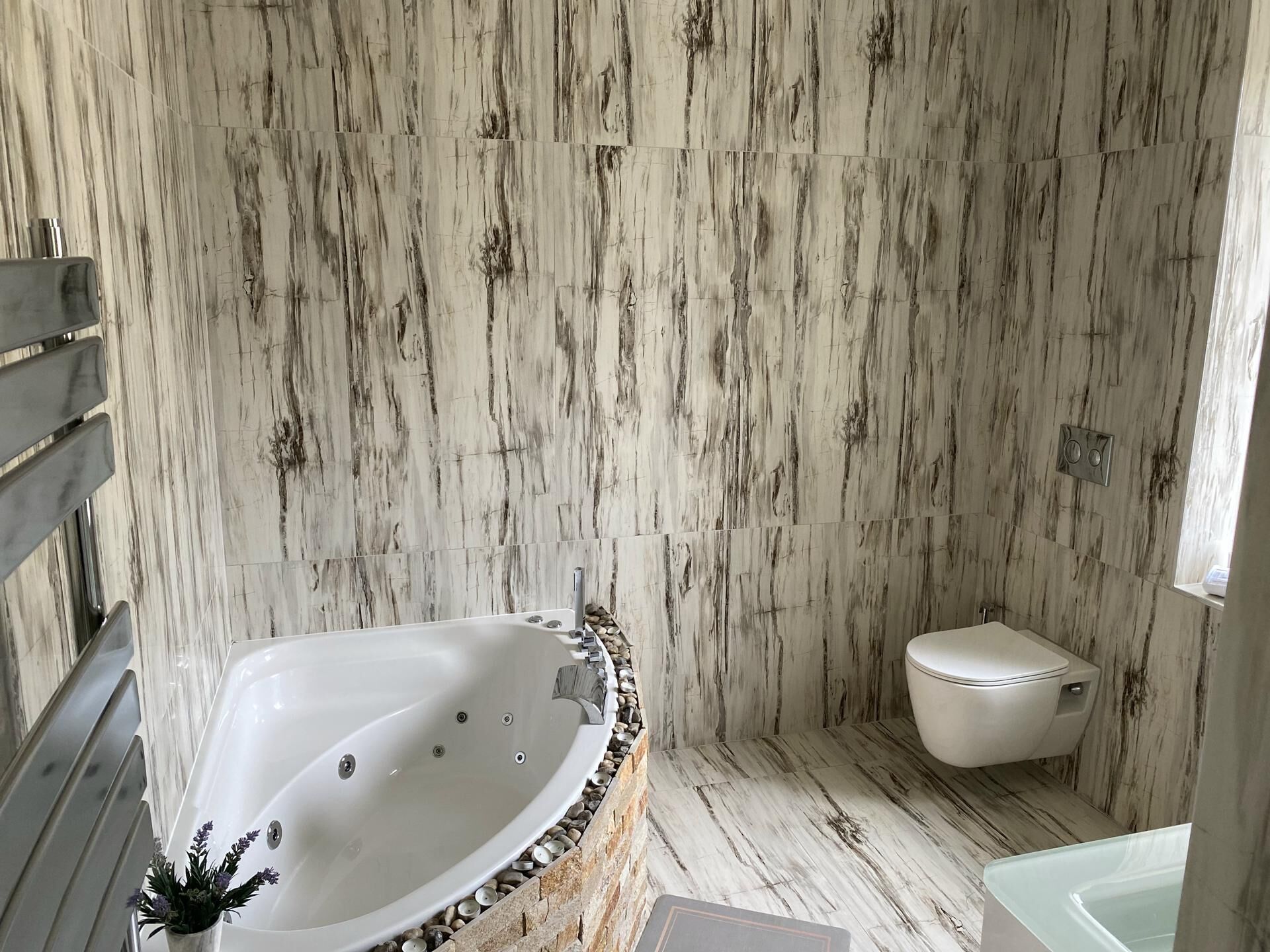 Un baño con pared de mármol, bañera, inodoro y zona de ducha.