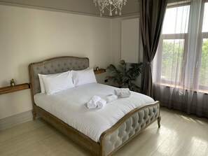 A neatly made bed with white linens and rolled towels, a wooden headboard, and a large potted plant beside the window. - Seaside Retreat at Port Talbot (Port Talbot)