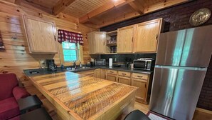 A wooden cabin-style kitchen with a central island, wooden cabinets, a stainless steel refrigerator, and a microwave. - Pluggy’s Place - Perfect Location |Outdoor Firepit (Beattyville)