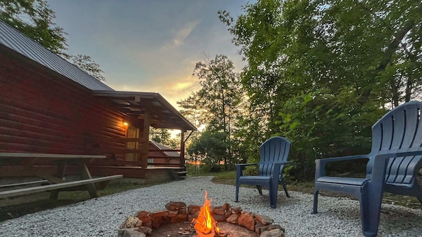 A fire pit surrounded by rocks, two Adirondack chairs, and a wooden cabin with a porch. - Pluggy’s Place - Perfect Location |Outdoor Firepit (Beattyville)