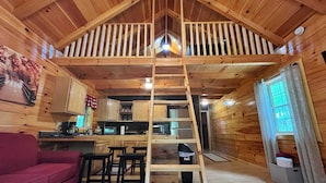 A wooden cabin interior with a loft bedroom, kitchen area, and a red sofa. - Pluggy’s Place - Perfect Location |Outdoor Firepit (Beattyville)