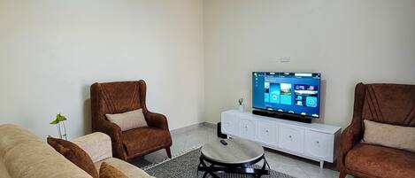 A living room with a beige sofa, two brown armchairs, a coffee table, and a TV on a white cabinet.