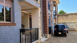A multi-story residential building with balconies, a paved driveway, and a parked SUV. - Elite Homes (Kampala)