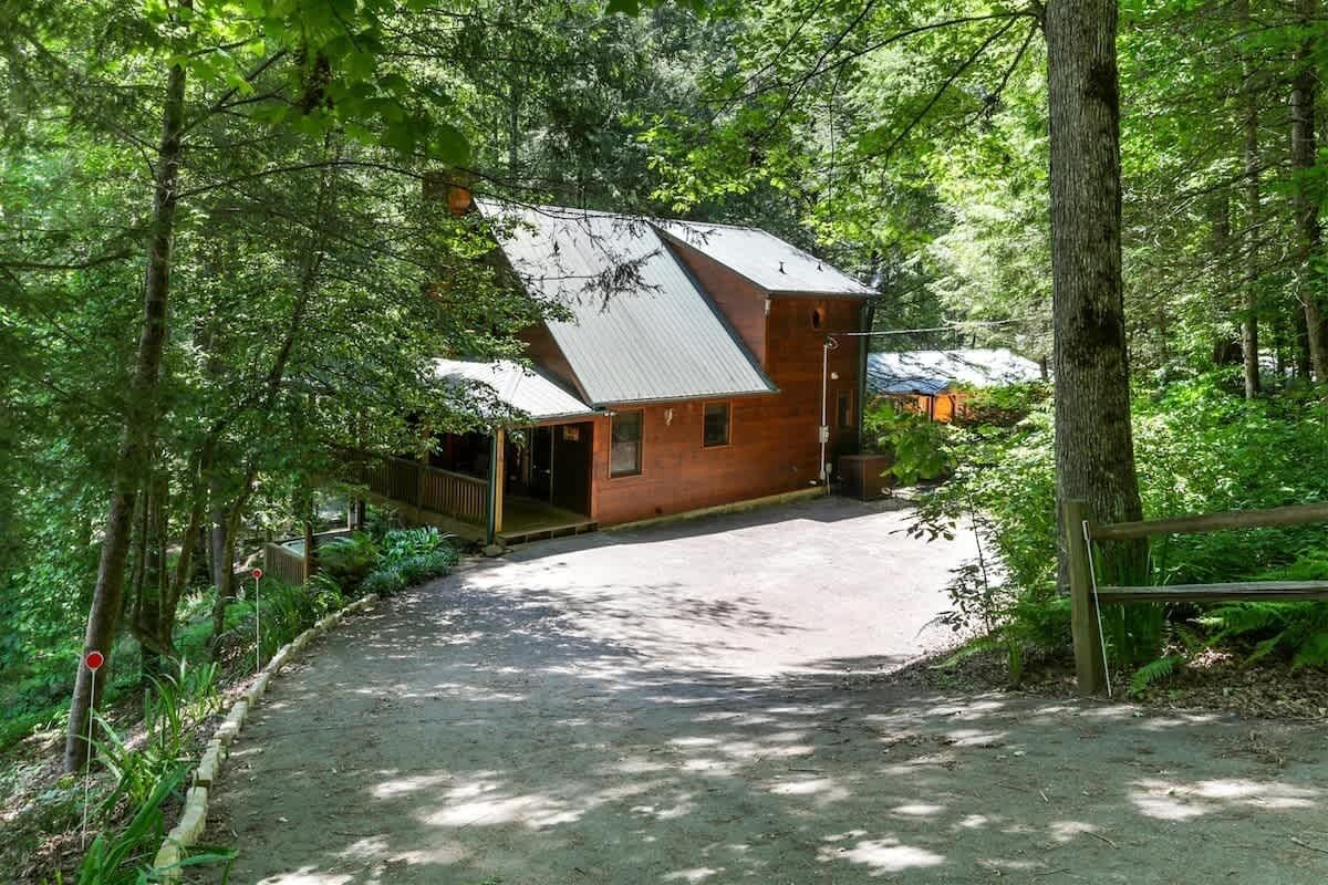A rustic cabin with a sloped roof, surrounded by dense forest.
