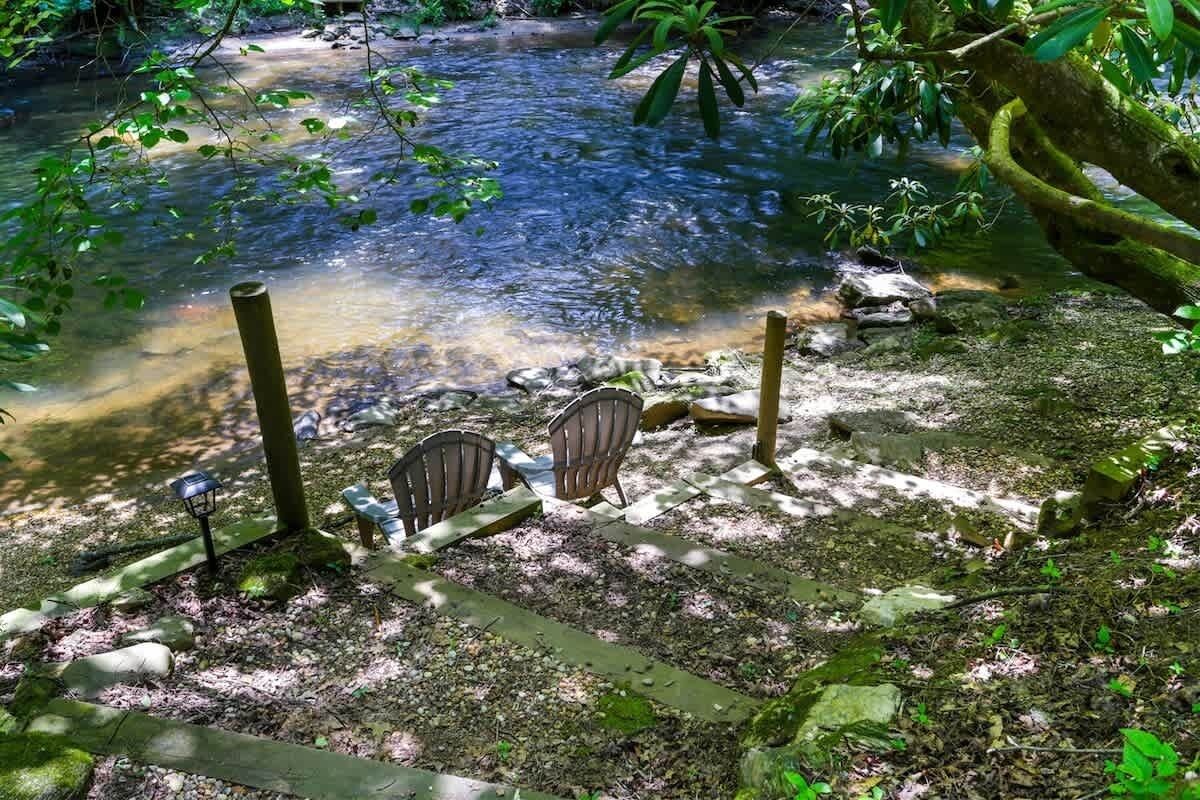 A serene outdoor seating area with chairs and a table, a small stream, and surrounding greenery.