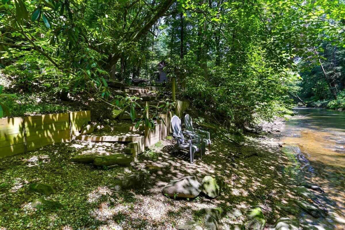 Un entorno tranquilo a orillas del río, con una terraza de madera, una silla y una pequeña construcción.