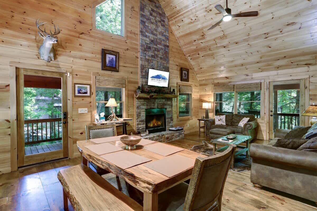 L’intérieur d’une cabane en rondins, avec une cheminée en pierre, des meubles en bois et une tête de cerf accrochée au mur.