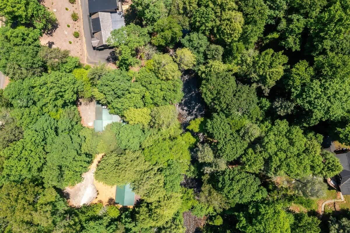 An aerial view of a property with dense greenery, a small pond, and a building with a sloped roof.