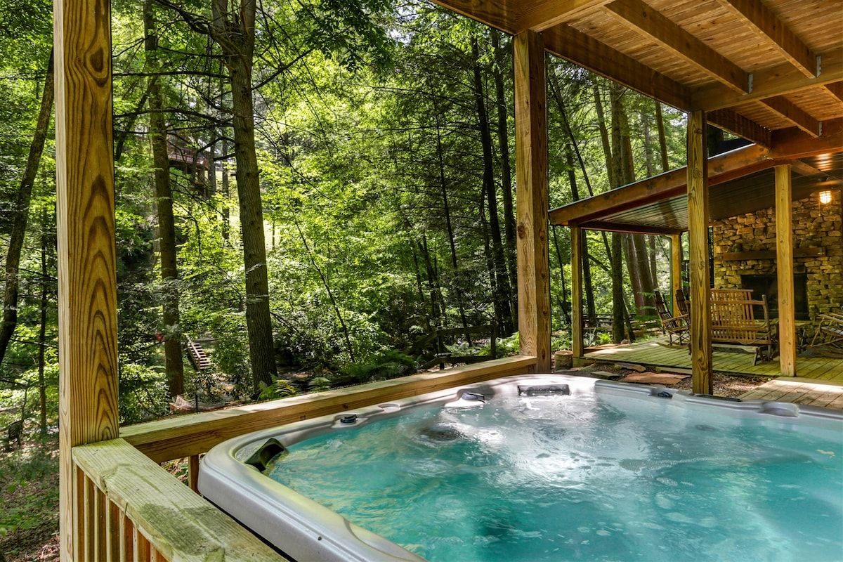 A hot tub surrounded by a wooden deck with a forest backdrop.