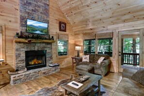 Un interior de cabaña acogedor, con una chimenea de piedra, un sofá cómodo y un televisor montado encima.