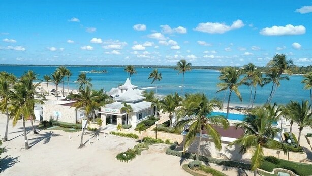 Un resort frente a la playa con piscina, palmeras y un club de playa.