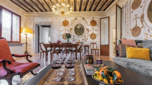 A dining area with a wooden table set with wine glasses, a fruit bowl, and a chandelier.