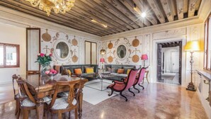 A spacious living room with a wooden ceiling, a dining area with a round table and chairs, and a sofa set.