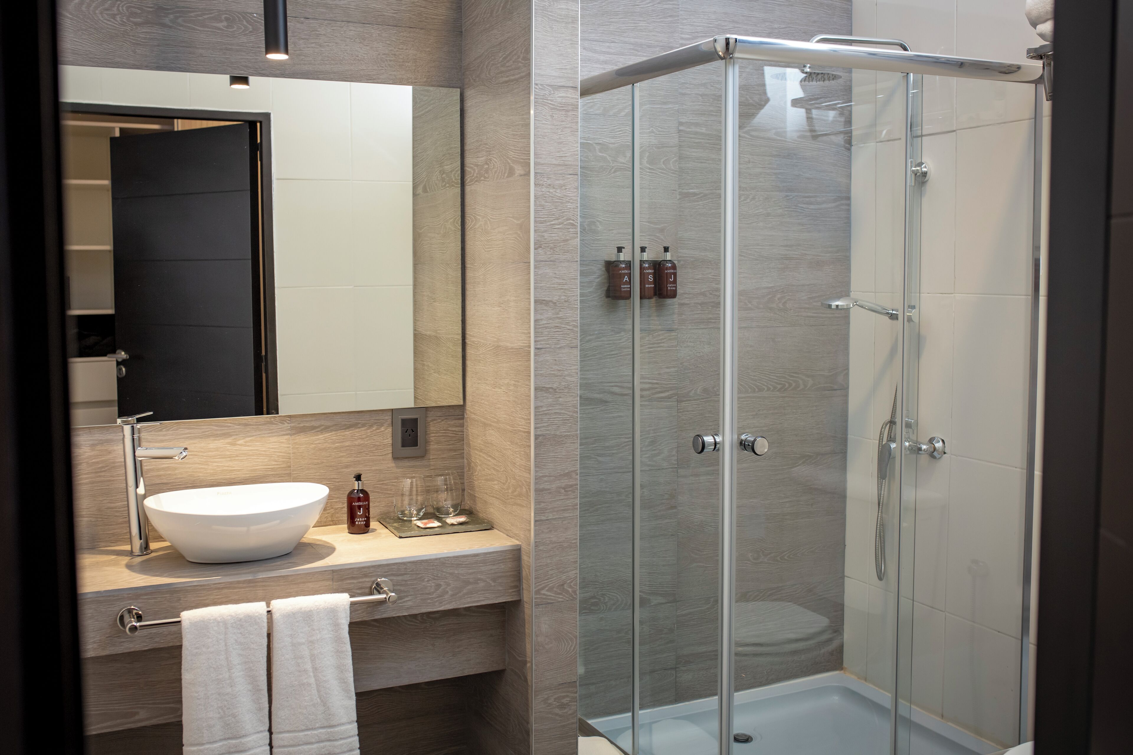 A modern bathroom with a large mirror, a vessel sink, and a glass-enclosed shower.
