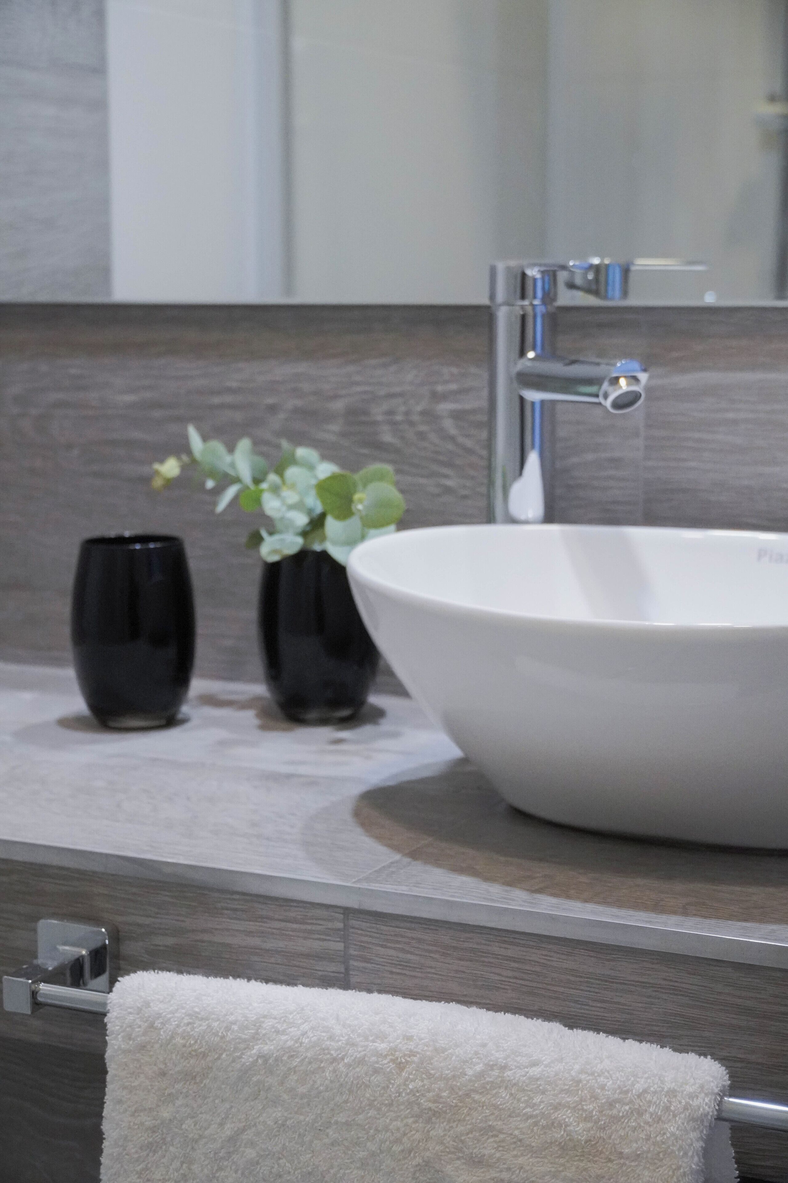 A bathroom with a white sink, two black vases with plants, and a towel hanging on a rack.