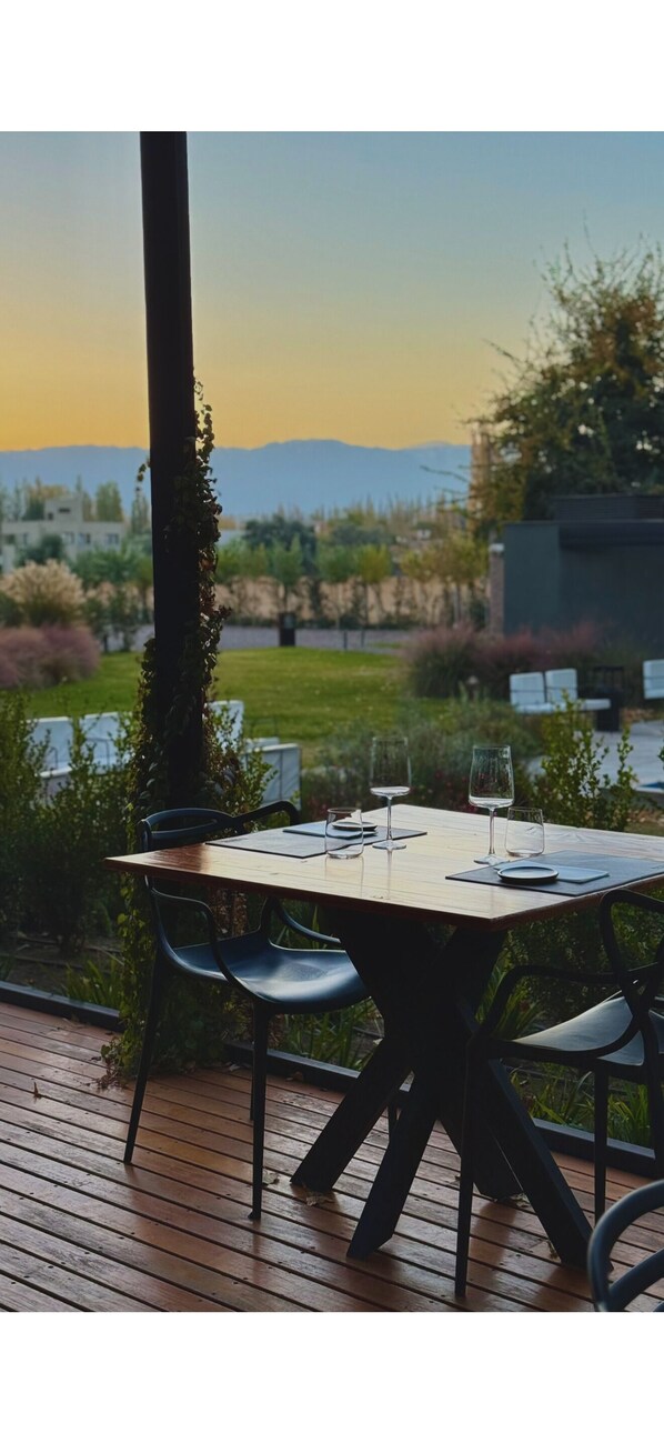 An outdoor dining area with a table and chairs, surrounded by greenery and a view of distant mountains.