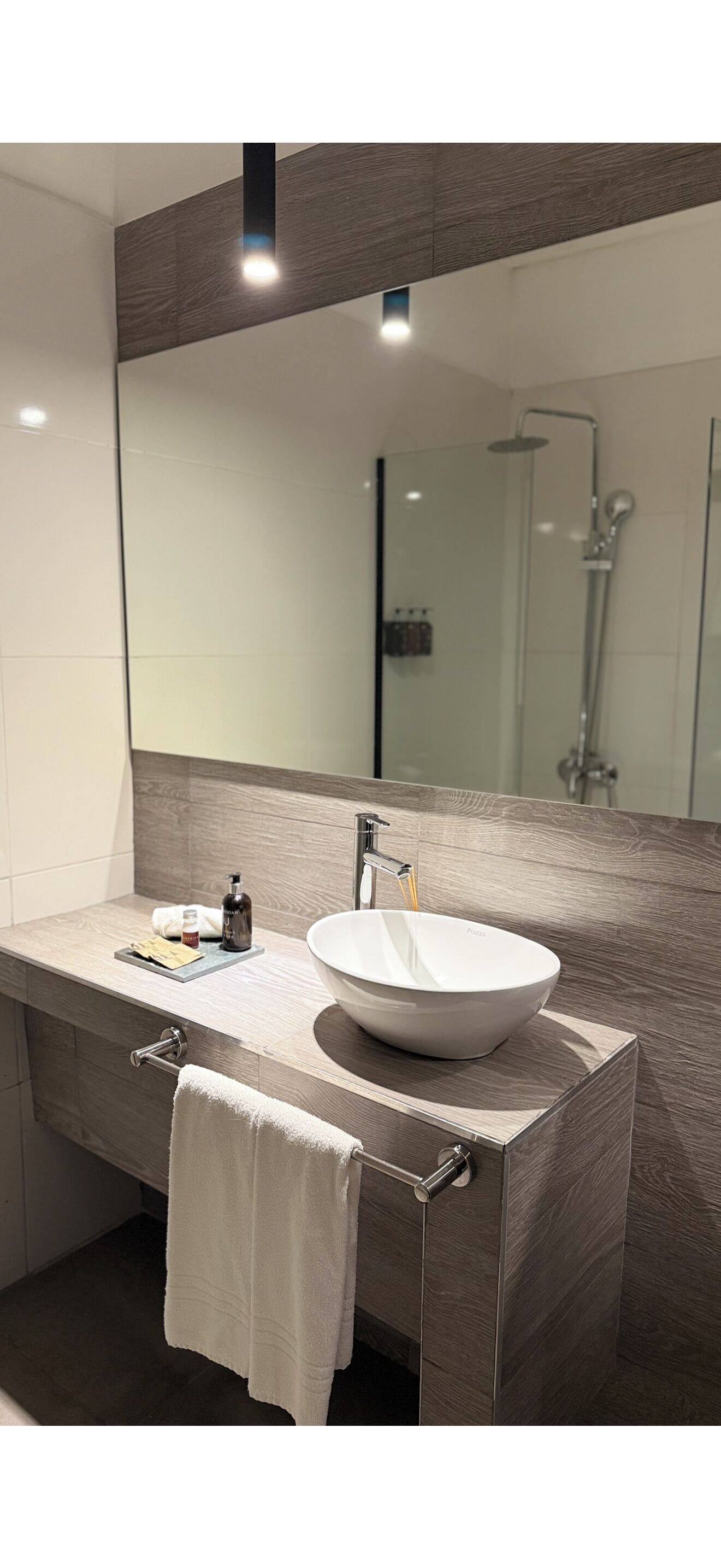 A modern bathroom with a large mirror, a white sink, and a towel hanging on the wall.