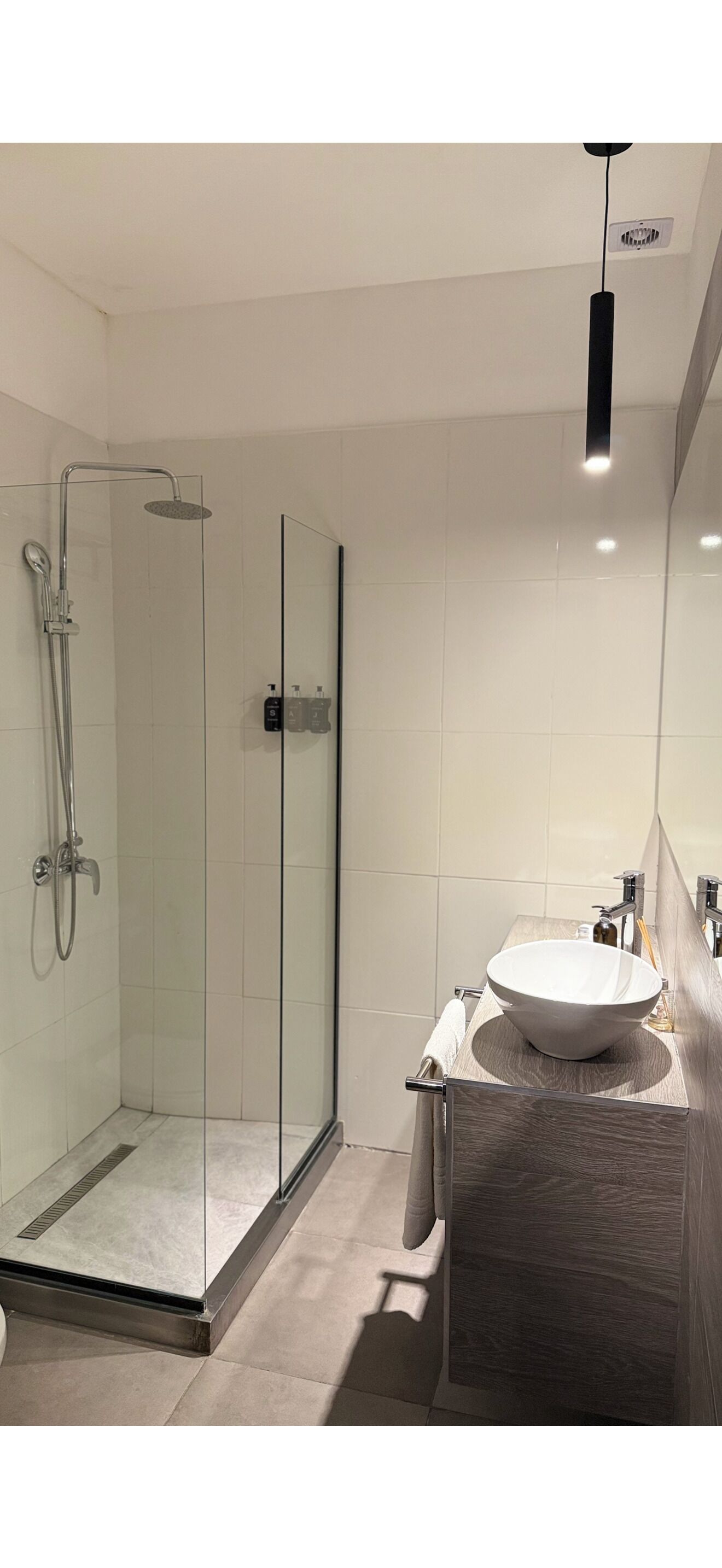 Ein modernes Badezimmer mit einer gläsernen Duschkabine, einem runden Waschbecken und einem hölzernen Waschtisch.