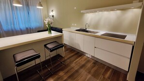 A modern kitchen with a white countertop, a stainless steel sink, and a built-in oven. There is a bar stool and a vase with flowers on the counter. - Domus Ballà Tonale Camera 1 (Verona)