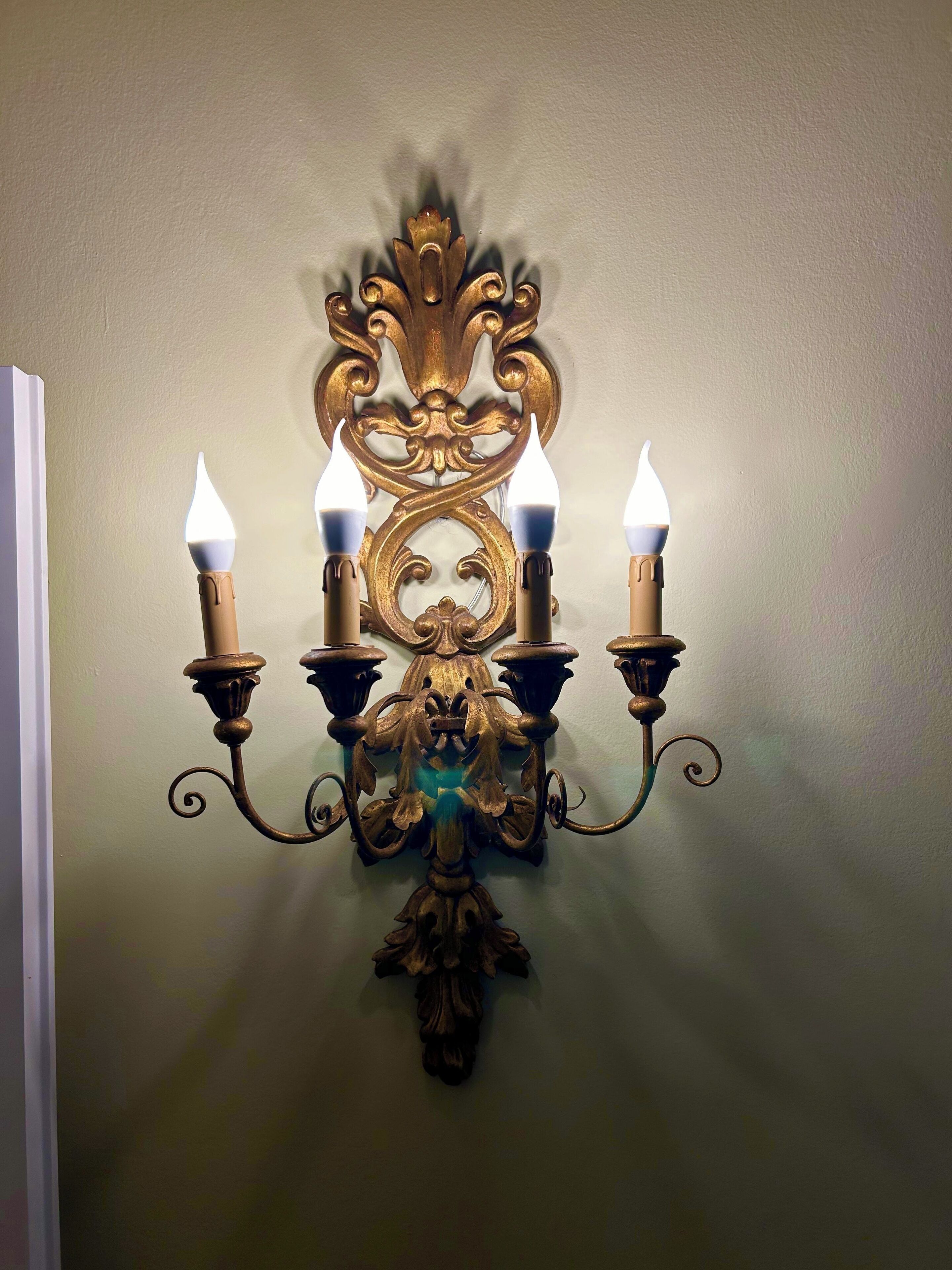 Eine wandmontierte Wandleuchte mit vier flammenartigen Lichtern und aufwendiger, goldfarbener Metallverzierung.