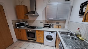 A compact kitchen with a microwave, stove, oven, washing machine, and sink. - City Center Gem (Liverpool)