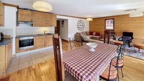 Une cuisine moderne avec des meubles en bois, un coin repas avec une nappe à carreaux et un salon confortable avec un canapé et une horloge au mur.