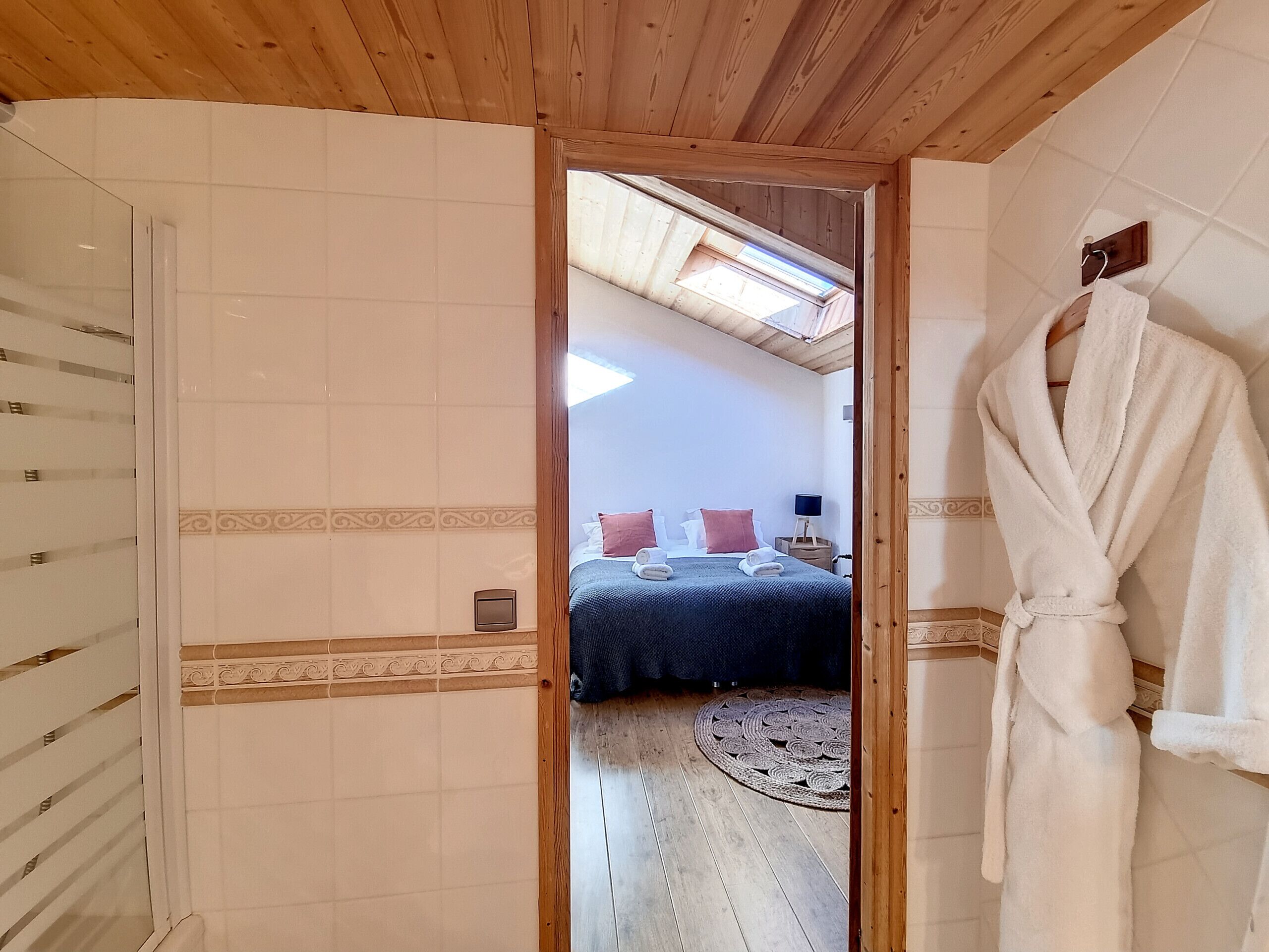 A bathroom with a wooden ceiling, a mirror, and a white robe hanging on the wall.
