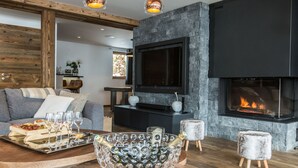 A modern living room with a fireplace, a large TV, and a glass bowl with champagne bottles. - Chalet Le Saint-Jean - 15 pers - proche pistes (Les Gets)