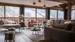 A cozy living room with a wooden floor, large windows with a snowy mountain view, and modern furniture. - Chalet Le Saint-Jean - 15 pers - proche pistes (Les Gets)