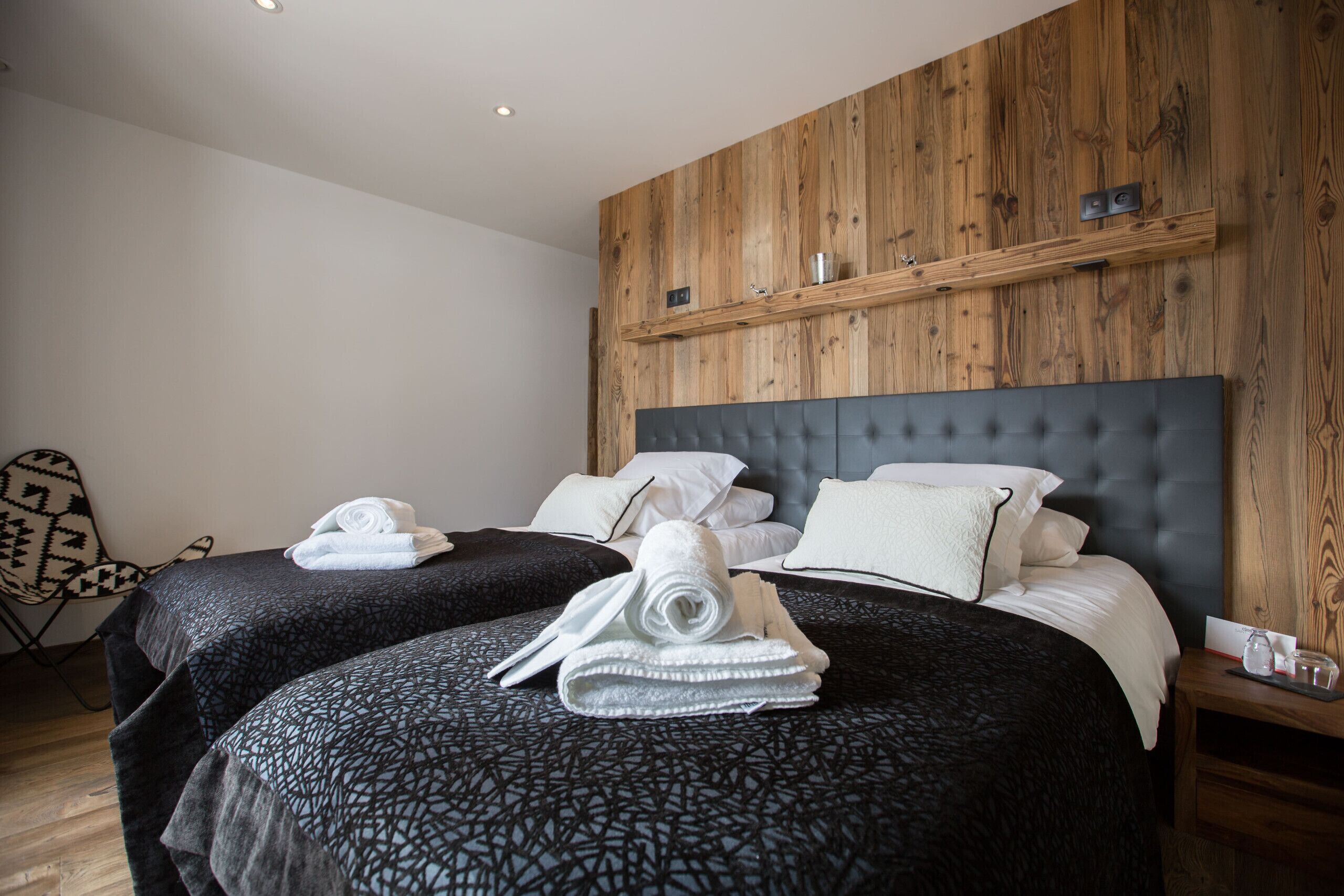 A hotel room with two beds, wooden paneling on the walls, and a small wooden nightstand.