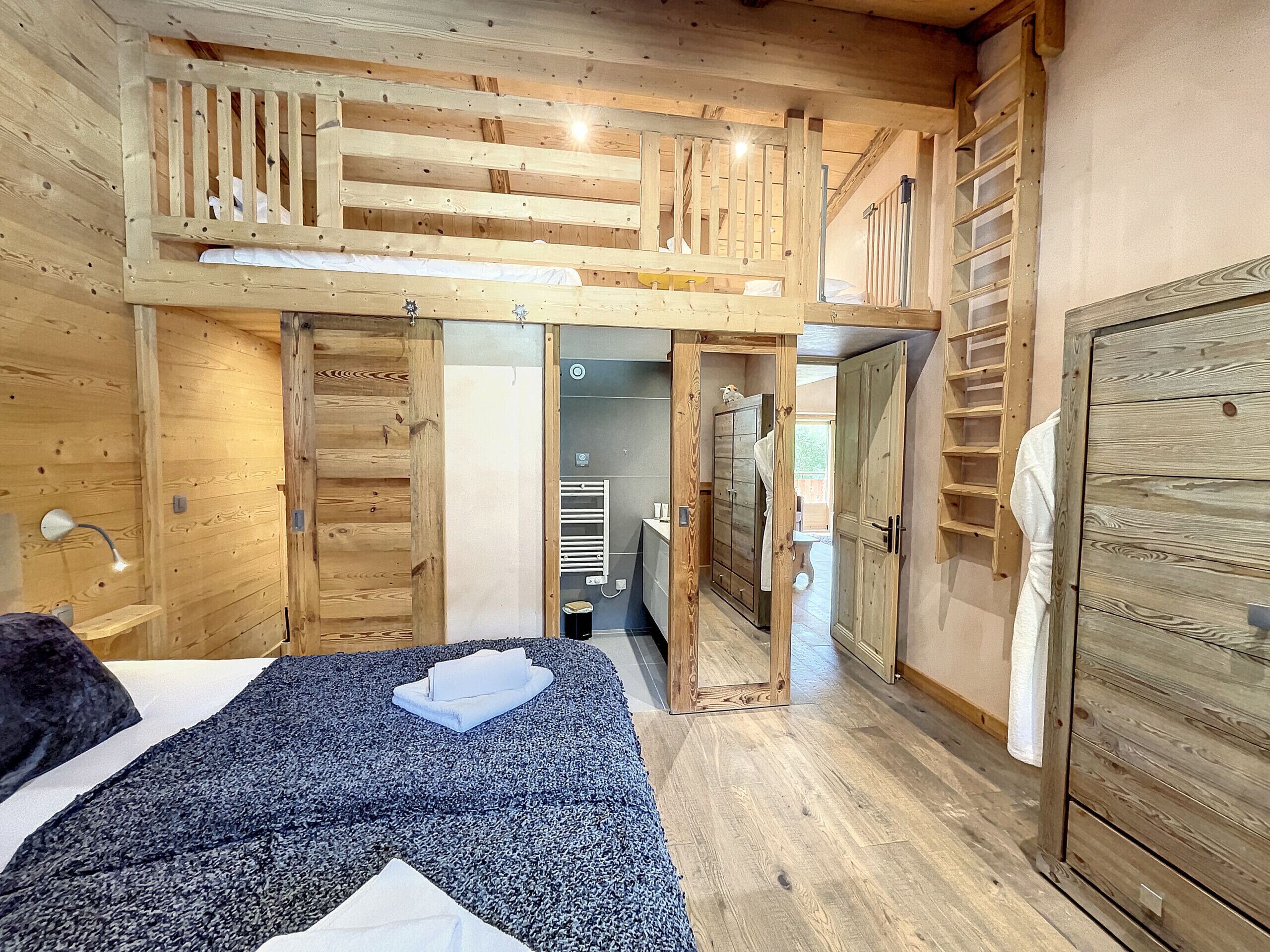 Un dormitorio de cabaña de madera con una cama litera, un vestidor y un baño visible a través de una puerta abierta.