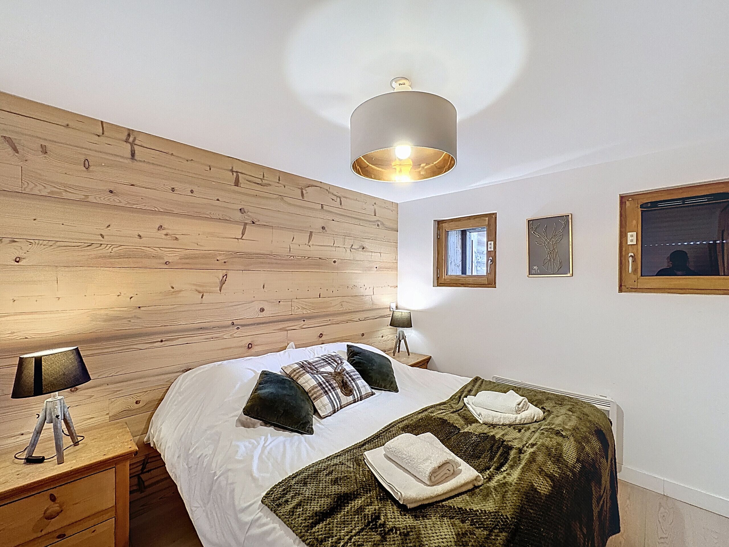 Ein Schlafzimmer mit einem hölzernen Kopfteil, einem Bett mit weißer Bettwäsche, zwei Nachttischen mit Lampen, einem Fenster und einer Wandleuchte.